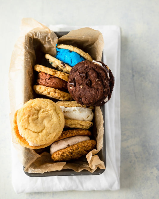 A selection of Cool Jacks colorful ice cream cookie sandwiches stacked on a parchment-lined tray with a white napkin.