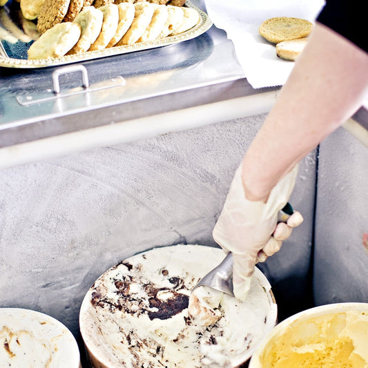 Gloved hand scooping ice cream next to trays of cookies at Cool Jacks dessert cart in backyard.