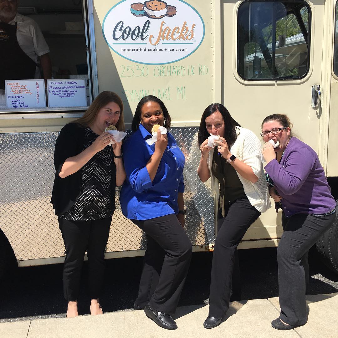 Four women smiling with Cool Jacks ice cream sandwiches in front of the Cool Jacks truck at a Michigan summer street fair.