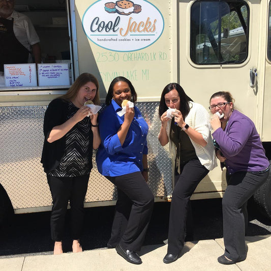 Four women smiling with Cool Jacks ice cream sandwiches in front of the Cool Jacks truck at a Michigan summer street fair.