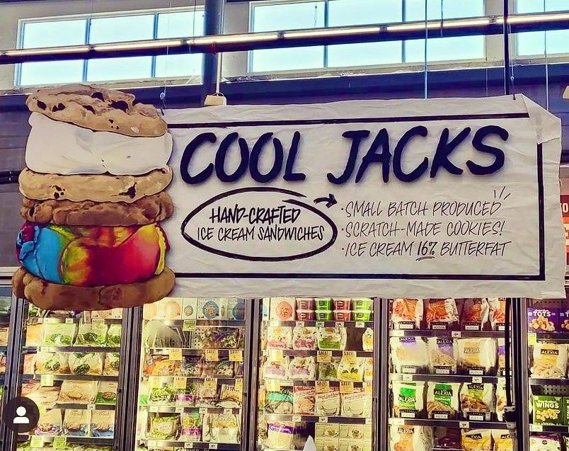 Cool Jacks banner above a freezer aisle showcasing a stack of handcrafted ice cream sandwiches and store display.