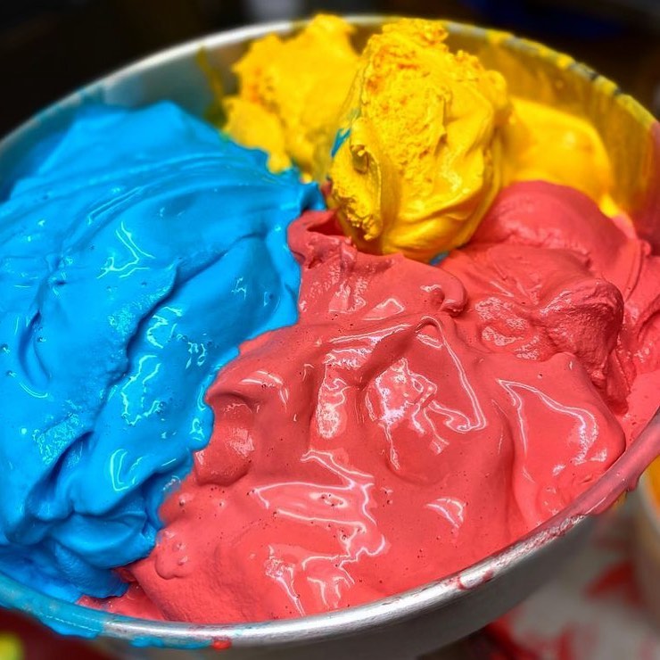 Bright blue, red, and yellow Cool Jacks ice cream scoops swirled together in a metal tub.